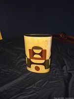 Full side view of the vase showing geometric shapes in brown, olive green, and beige on an oval body.