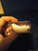 Front and top angled view of the small white ceramic rabbit figure held in a hand inside clear plastic packaging.