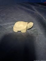 Small turtle figurine on dark fabric background showing shell and body details.