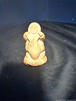 Front view of soapstone carving figurine showing figure with detailed face and hands on chest.