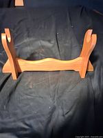 Wooden sword stand on a dark cloth background, showing curved arms and stable base.