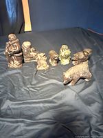 Photo showing all seven soapstone carvings displayed on a dark surface, including human and animal figures.