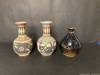 Group of 3 pottery vases including two tall patterned vases and one smaller dark glazed vase.