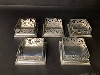Five pewter square candle holders arranged in a group showing decorative cutout pattern and square bases.
