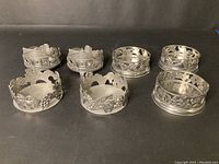 Photo showing all seven pewter candle holders arranged on a black surface, highlighting the variety in designs and shapes.