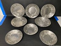 Eight pewter bowls arranged with grape vine design, showing both sizes.