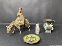 Four items arranged in a row: bronze figure of man on horse, small stone seal, bronze incense burner, and cloisonné dish with dragon on green background.