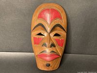 Full front view of carved wooden mask showing painted red and black geometric designs