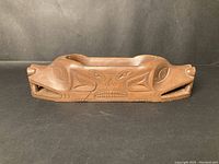 Front view showing detailed hand carved wooden dish with animal heads at each end and a carved stylized face in the center