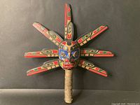 Full front view of carved rattle showing face, radiating blades and wrapped handle