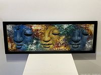 Full view of the framed original artwork showing the triptych of three faces in blue and gold hues.