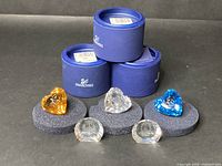 Five Swarovski crystal figurines displayed with original blue round boxes, sitting on black foam pads.