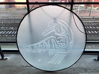 Front view of the circular etched glass panel with visible West Coast Indigenous bird design, hanging against a window.
