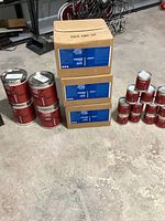 Photo showing multiple unopened cans and boxes of ArmorPoxy epoxy coatings in various sizes including metal cans and cardboard 2 gallon kits.