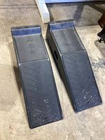 Pair of black plastic ramps placed on concrete floor showing overall size and shape with slight surface wear.