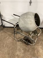 Concrete mixer in wheelbarrow style with large rotating drum resting on the floor showing overall condition and general structure with handles and wheels.