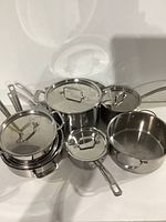 Overview of 7 stainless steel cookware pieces with lids on some items, showing handles and overall set condition.
