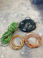 Four coiled extension cords in green, black, yellow, and orange on concrete floor.