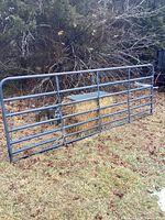Full view of the metal farm gate outdoors showing rectangular shape with horizontal bars and worn gray-blue paint.