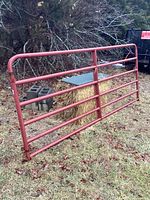 Full view of the red metal Tarter farm gate resting on grass, showing overall size and condition.