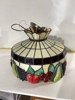 Full view of stained glass light fixture with fruit designs on lower section and geometric pattern on upper section.