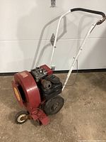 Front view of the Giant Vac blower showing red blower housing, black gas engine, white metal handle, and one wheel.
