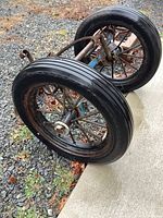 Two large spoked metal wheels with black rubber tires on rusted metal frame angled on ground showing tread and frame details.