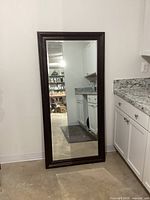Full view of the large wall mirror with dark wood frame standing against a wall in a kitchen area.