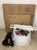 Overview photo showing three flat cardboard moving boxes, a large roll of bubble wrap, two packing tape dispensers, and the black shoulder carry strap.