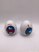 Front view of two white ceramic Snoopy eggs with colorful illustrations and copyright dates