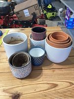 Photo showing various ceramic plant pots on a wooden surface including plain white, terracotta nested pots, and textured patterned pots.