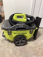 Ryobi 18V cordless wet dry vacuum with black hose coiled on top and attached accessories, positioned on a floor.
