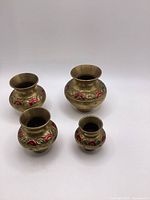 Four small brass decorative pots arranged on a white surface, showing overall size and decorative painted detailing.
