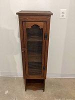 Front view of small wooden pie safe cabinet showing door with decorative mesh and wooden knob, standing on floor against wall.