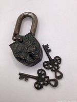 Front view of bronze padlock showing embossed seated figure and two skeleton keys
