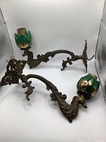 Two ornate vintage metal wall sconces with decorative green and gold candle holders shown on a white background.
