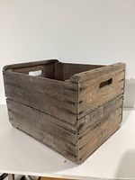 Three angled views of a vintage wooden crate showing its rustic construction, cutout handles, and stenciled text.