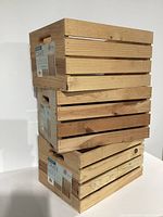 Stack of three natural wooden storage crates with labels and handle cutouts