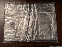 Photo of the folded clear plastic table cover sealed in plastic packaging, showing the item is new and unopened.