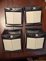 Four Claoner solar outdoor fence lights with motion sensors and LED panels shown from the front on a wood surface.