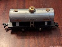 Front view of silver Lionel Lines tanker train car with rivet details and brass cap on top, mounted on black base with wheels.