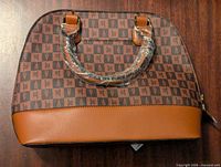 Front view of London Fog satchel crossbody bag showing logo pattern and tan leather-like bottom trim.