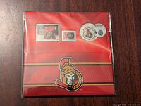 Front view of the red presentation card with two Ottawa Senators stamps and commemorative coin visible in plastic packaging, with team logo at bottom.