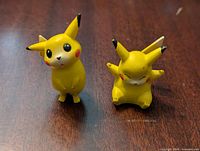 Two yellow Pikachu figures on a wooden surface, one standing and one sitting, showing overall condition and details