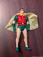 Front view of Robin action figure showing red torso with 'R' logo, green gloves and boots, yellow cape, and facial paint details.