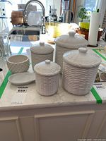 Set of five white ceramic canisters with a basketweave texture, different sizes placed on countertop.