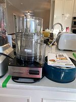 Front and side view of Cuisinart food processor including base, mixing bowl with lid, blade inside, manual, and accessory container.