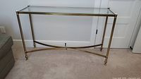 Full frontal view of glass and brass side table showing rectangular beveled glass top and brass legs with cross braces.