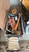 Photo showing various hand tools including C-clamp, saws, axe, hammer, and metal level all arranged in a tray with a coiled wire roll.
