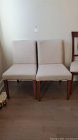 Front view of two beige fabric covered occasional chairs with wooden legs placed side by side.